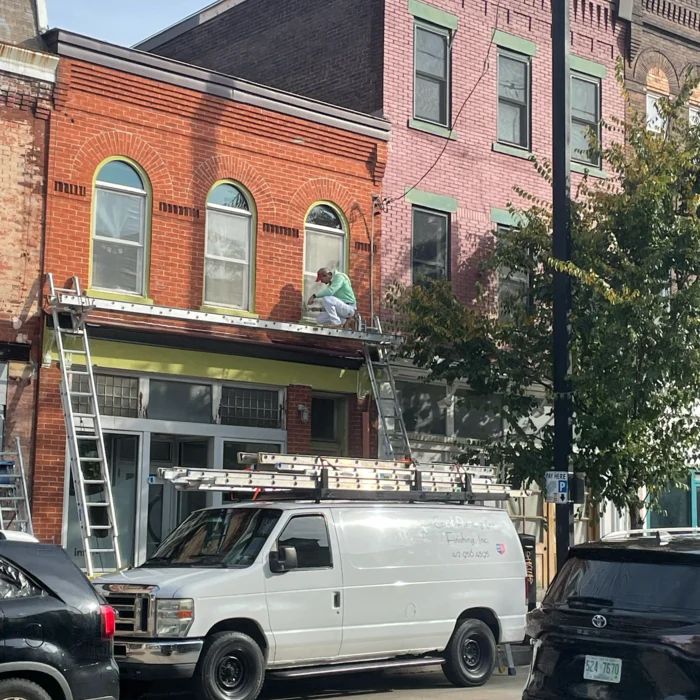 Caridi painter on staging refinishing the brick and arched window trim of a storefront