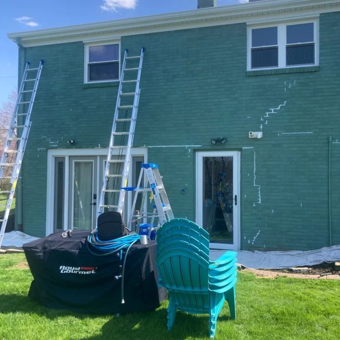 The same house before painting, in faded sea green with ladders set for prep
