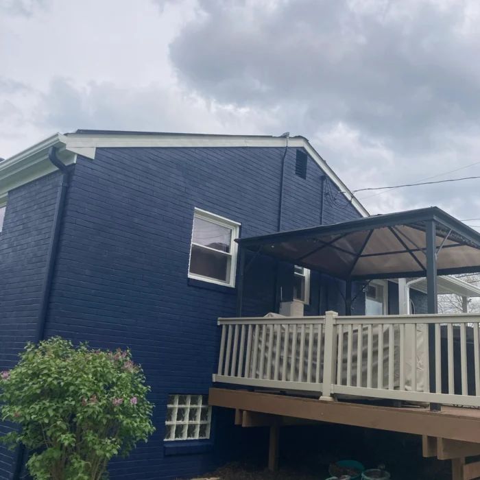 Side elevation of a navy brick home with white gutters, rake board and a painted deck rail