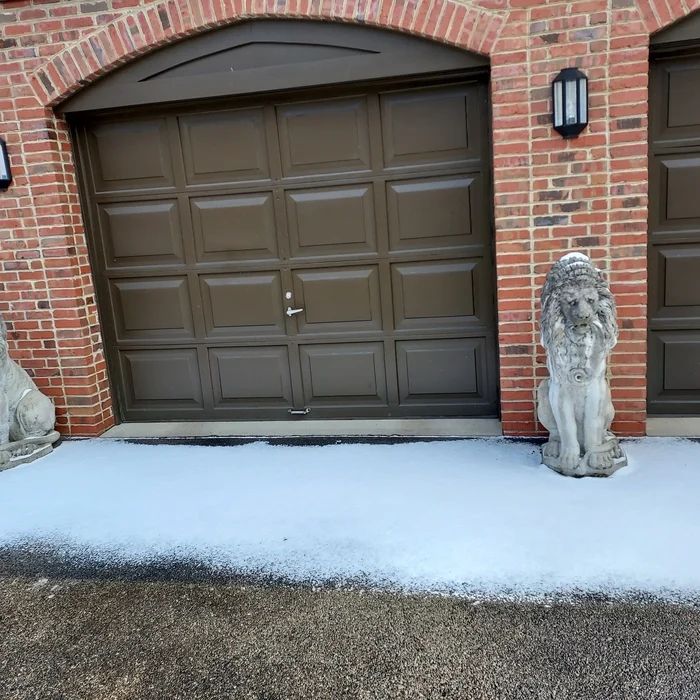 Brick garage bay with a freshly refinished bronze garage door and a stone lion beside it