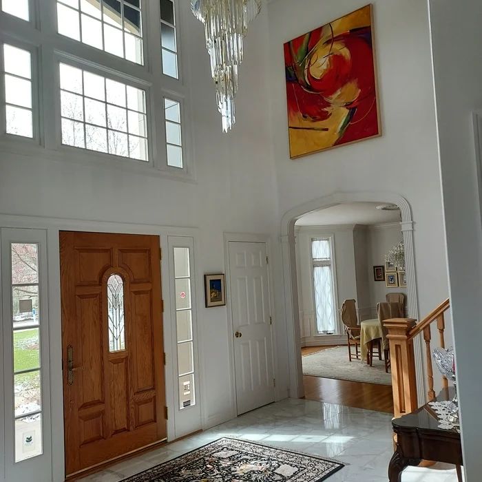 Bright white two-story entry foyer with a chandelier, oak front door and marble floor