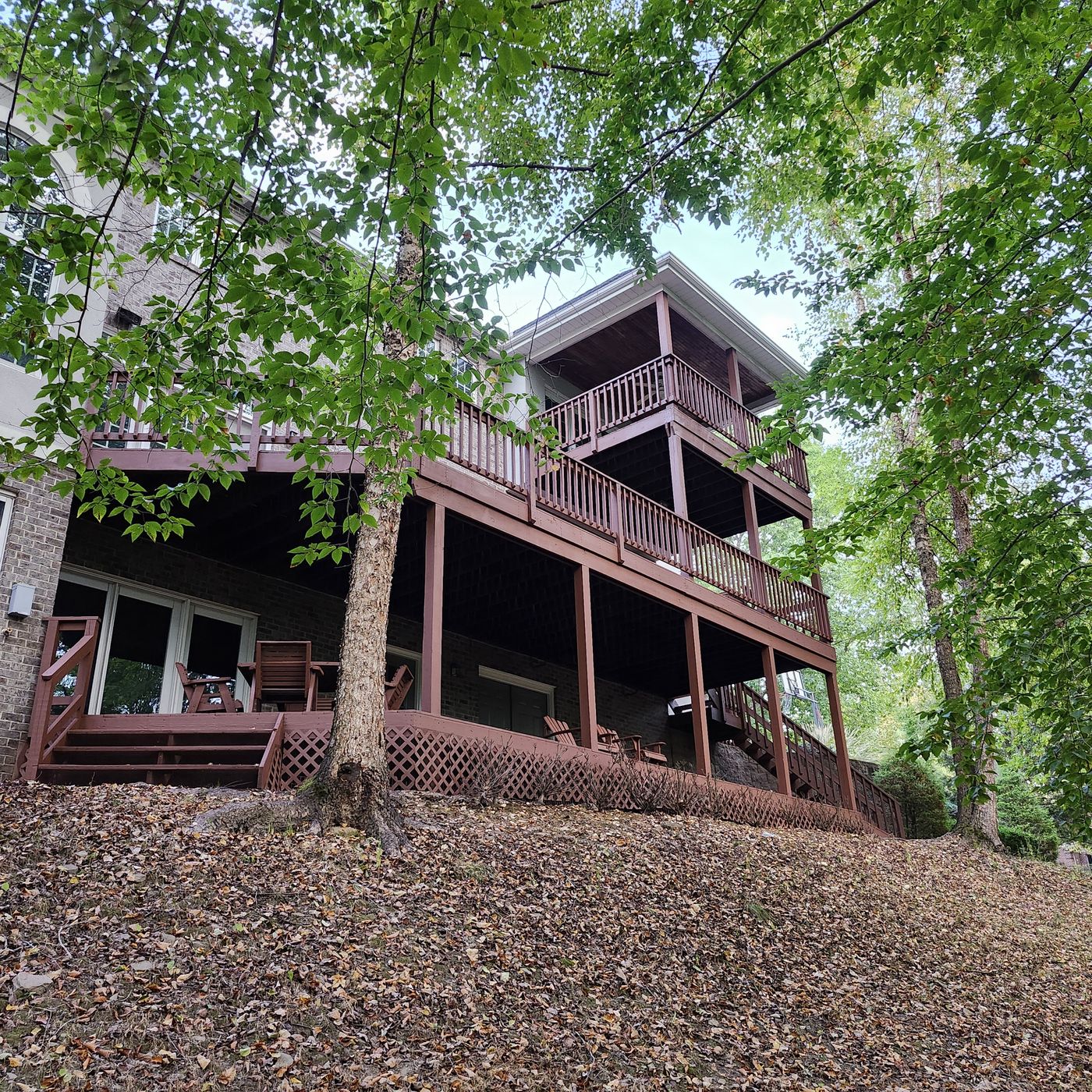 Three-level wood deck on the back of a brick home in the woods, freshly restained a deep red-brown